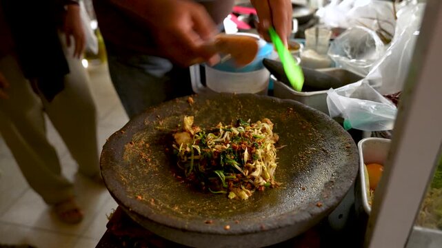 Making A Lotek Kupat Dish with Peanut Sauce and Vegetables In A Large Mortar And Pestle. - closeup shot