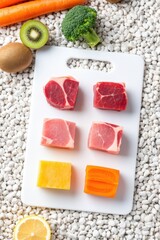 Raw meat cutlets and fresh fruits on a white cutting board over gravel. Use: cookbook photography, food blog header, healthy meal prep.