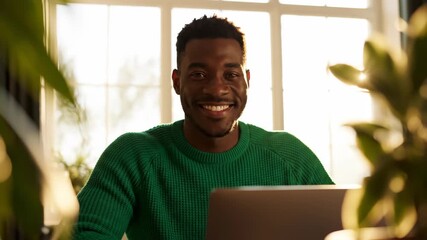 Happy young adult black man working on a laptop in a bright sunlit home office. Composite image showing a successful freelancer smiling during a remote work session