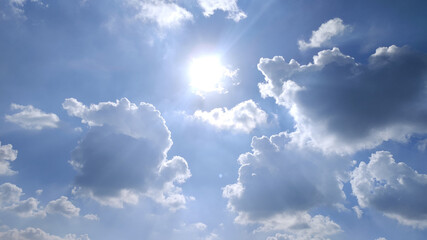 Bright Sun Shining Through Fluffy Clouds Over Clear Blue Sky Creating Serene Daylight Scene.