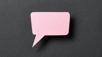 Pink cut out paper speech bubble with shadow and copy space for text on dark background, close-up flat lay top view conceptual backdrop