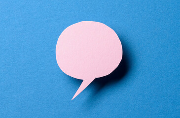 Pink blank cut out paper speech bubble with shadow and copy space for text on blue background, close-up flat lay top view conceptual backdrop
