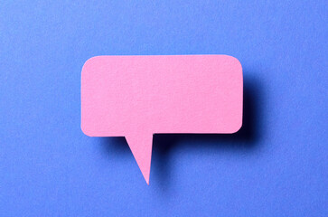 Pink blank cut out paper speech bubble with shadow and copy space for text on blue background, close-up flat lay top view conceptual backdrop