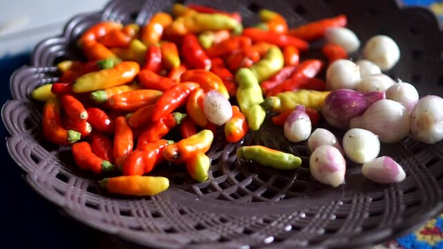 Fresh red chili peppers and small shallots on a plate, ready to be used as cooking ingredients.