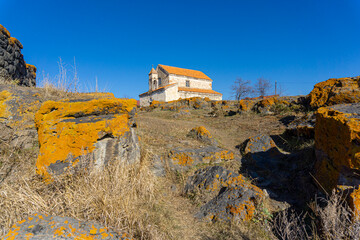 The church with its bell tower illuminated by the bright sun. The fence walls, made of large stones, are covered with bright brown lichen in the courtyard. Saro, Meskheti, Javakheti, Georgia.