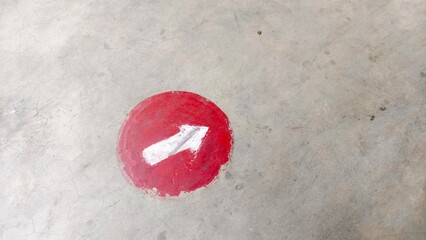 Red direction arrow painted on concrete floor, ideal for navigation signs, safety guidance, urban design, and editorial use. Perfect for buyers in transportation, public facilities, education, and way