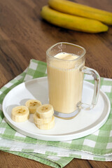 milkshake with bananas, thick delicious drink in a ribbed mug. fruit dessert on the table and banana rings on a plate
