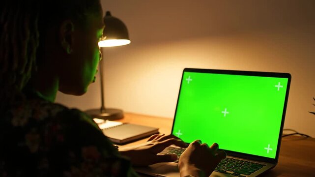 A Woman Works Late At Night On Laptop With Green Screen Display