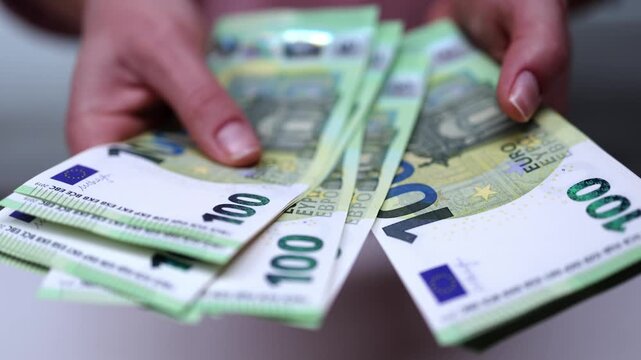 Hands holding a stack of euro banknotes, displaying multiple 100 euro bills, showcasing the gradual release and arrangement of currency in a close-up view