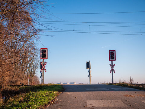 Railway level crossing without barriers with red warning lights and crossbuck signs. Red light means do not cross. Rural road and rail intersection under clear blue sky.