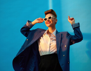 Modelka w stroju z lat 80 tych i uczesaniu w stylu retro pozuje do zdjęcia na niebieskim tle