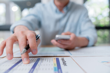 Businessman pointing at budget report and financial documents while holding a smartphone. Concept of financial analysis, business planning, and budget management in modern office.