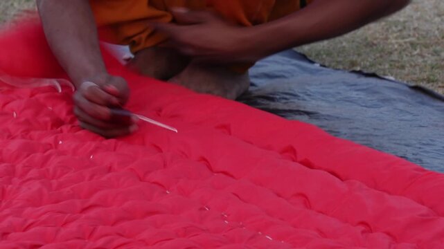 Rural Artisan Stitching Vibrant Red Quilt on Field