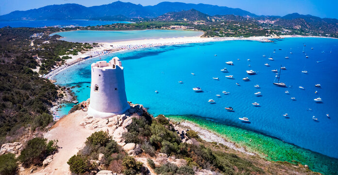 Ancient Saracen tower overlooking the turquoise waters of Porto Giunco beach in Villasimius, Sardinia. Aerial view of the historic coastal watchtower and crystal clear Mediterranean sea.