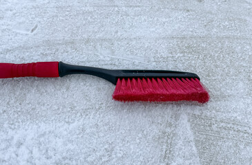 Removing snow from a car window with a brush with red bristles close-up on a sunny, frosty day. Cleaning and clearing the car from snow on a winter day. Snowfall, and a severe snowstorm in winter.