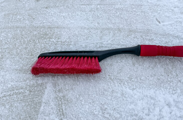 Removing snow from a car window with a brush with red bristles close-up on a sunny, frosty day. Cleaning and clearing the car from snow on a winter day. Snowfall, and a severe snowstorm in winter.