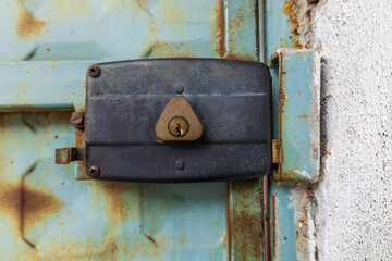 Old metal door lock mounted on weathered blue steel door with rust texture, close-up of industrial security hardware