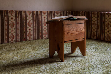 Open book resting on a small wooden table in a traditional interior with patterned fabric seating, calm reading and study atmosphere