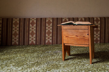 Open book resting on a small wooden table in a traditional interior with patterned fabric seating, calm reading and study atmosphere