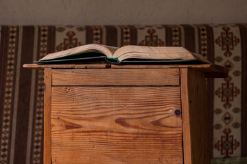 Open book resting on a small wooden table in a traditional interior with patterned fabric seating, calm reading and study atmosphere