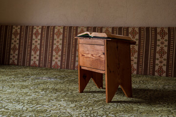 Open book resting on a small wooden table in a traditional interior with patterned fabric seating, calm reading and study atmosphere