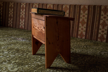 Green hardcover book with gold detailing placed on a wooden stand in a traditional interior, shallow depth of field and calm atmosphere