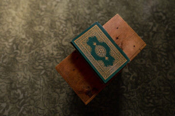Green covered book with ornate gold details resting on a wooden stand, top view with patterned carpet background and calm spiritual mood