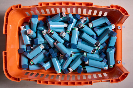Blue salbutamol asthma inhalers collected in orange plastic box, medical respiratory treatment equipment indoors. Concept of asthma care, emergency healthcare, and pharmaceutical supply