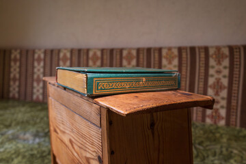 Green hardcover book with gold detailing placed on a wooden stand in a traditional interior, shallow depth of field and calm atmosphere