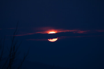 Dramatic sunset with the sun partially hidden by dark clouds, creating a moody sky and minimal atmospheric landscape