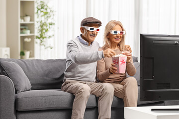 Mature couple wearing 3D glasses, eating popcorn and watching a movie