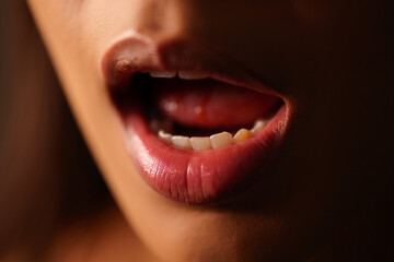 Close-up of a person's open mouth with glossy, vibrant lips, revealing white teeth and a tongue. Evokes emotion, expression, and oral health concepts.