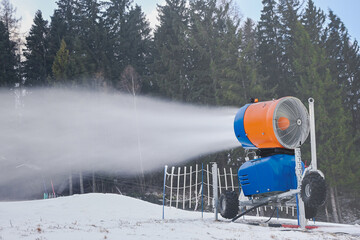 Snow cannon producing artificial snow on a ski slope surrounded by pine trees