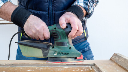 Craftsman. Adult carpenter using an electric sander to smooth an old wooden window. Construction industry, carpentry, housework do it yourself. Restoration.