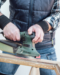 Craftsman. Adult carpenter using an electric sander to smooth an old wooden window. Construction industry, carpentry, housework do it yourself. Restoration.