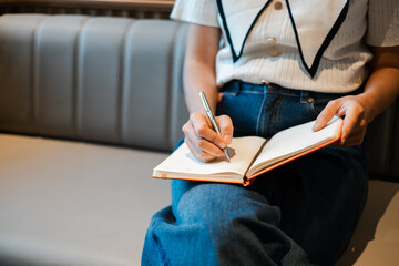 Close-up of a woman writing in a notebook while sitting on a sofa, capturing a moment of creativity and relaxation.