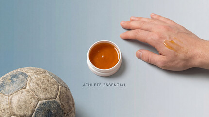 An athlete's hand applies a golden balm for muscle recovery after a football game. The balm is in a jar and a ball is beside.