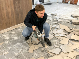 Removing a concrete floor with a hand hammer. Concrete rubble on the construction site of a house. Destruction of old tiles. Male construction removes the old tile from the floor with a hammer drill.