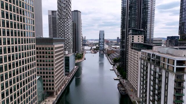 Backward aerial view along an urban river, rising to reveal modern skyscrapers. Cinematic drone shot showing contemporary architecture, glass towers and a metropolitan city skyline.
