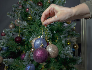 Woman holding Christmas ornaments in hands near decorated tree in cozy home interior