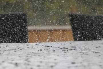 Close-up of heavy rain falling on a table on the terrace, the raindrops bursting into crowns.