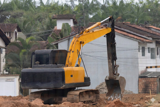 Yellow hydraulic excavator at a construction site with residential background
