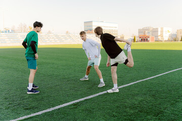 Three friends engage in a warm-up routine on a sunny soccer field, stretching and laughing...