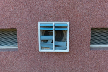 Ventilation grill on a textured wall showing signs of wear and age under bright sunlight