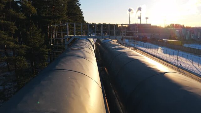 Glistening metallic conduits under bright sunlight cast elongated shadows over snowcovered forest surroundings