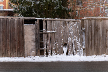 Weathered wooden fence stands against a cold winter backdrop, showcasing natures quiet charm in a snowy urban neighborhood