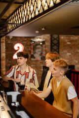 Fototapeta premium Three friends gather at a stylish bar, seated on high stools. They are engaged in conversation while sipping on their drinks, surrounded by a vibrant atmosphere and warm lighting.