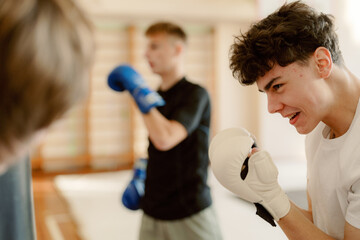 Two energetic young men practice boxing techniques in a bright gym. They focus intensely on their movements, showcasing determination and teamwork during afternoon training.