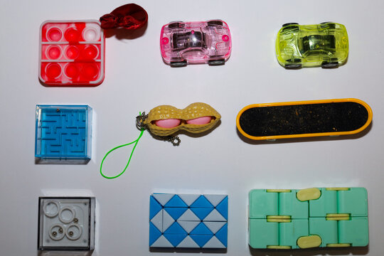 Collection of various anti-stress toys and small children's accessories neatly arranged on a bright surface. The set includes colorful puzzles, mazes, cars, and popular fidgets,