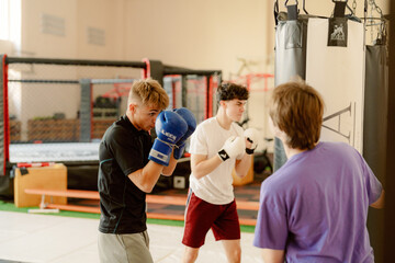 Three young boxers engage in a focused training session inside a gym. They each wear gloves and practice their techniques in an energetic atmosphere, surrounded by training equipment.